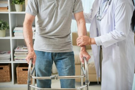 unrecognizable-female-doctor-helping-male-patient-walk-with-walking-frame_1098-20659